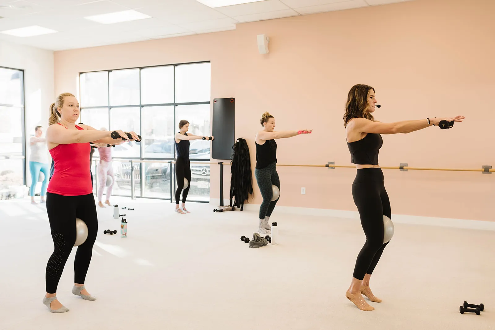 An instructor in a headset leading a small class with barre balls in the peach studio