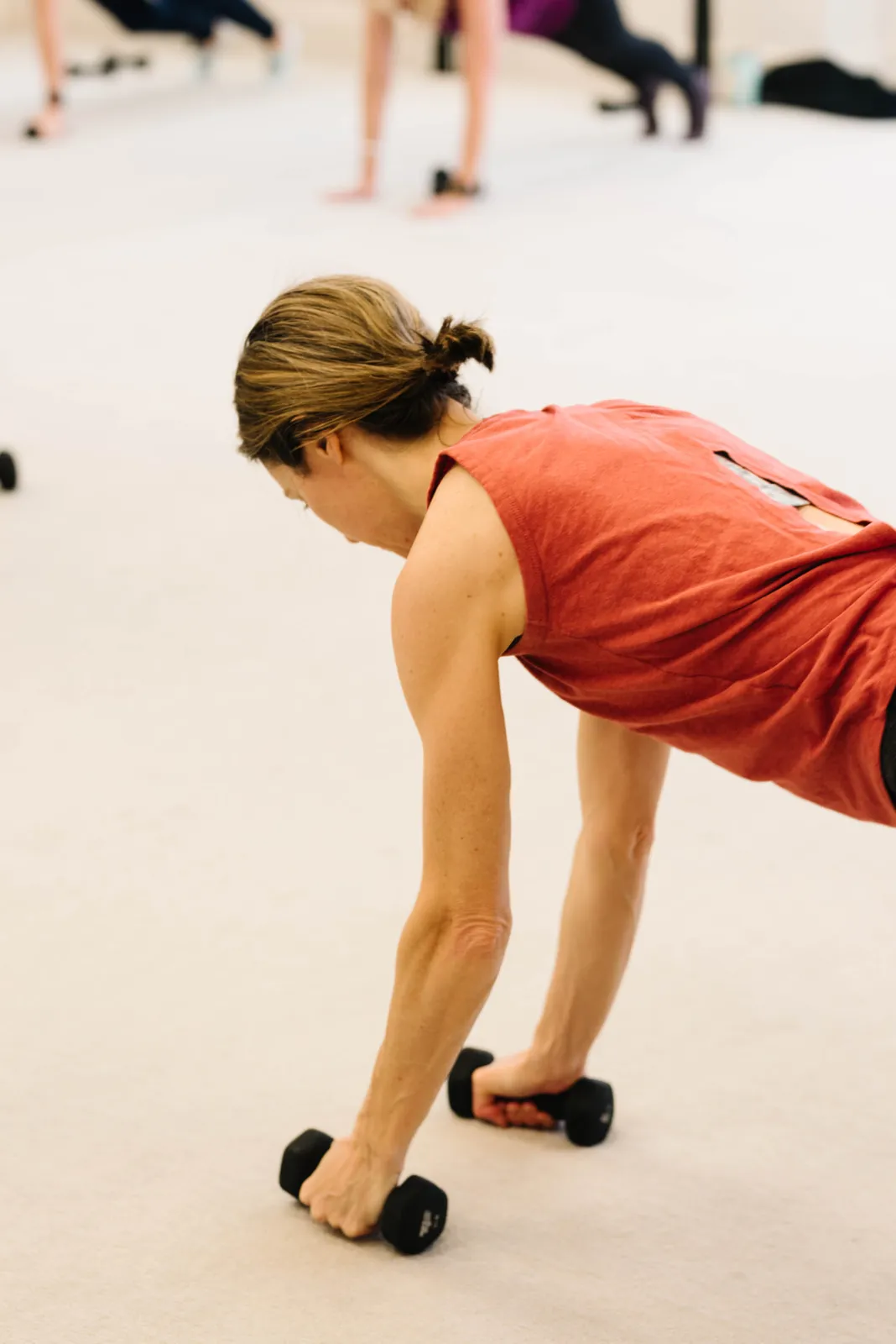 A client in a red tank folding forward over hand weights during upper body work