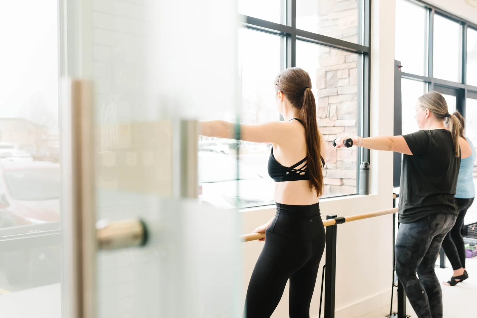 Clients working with light weights at the barre beside the studio's tall front windows