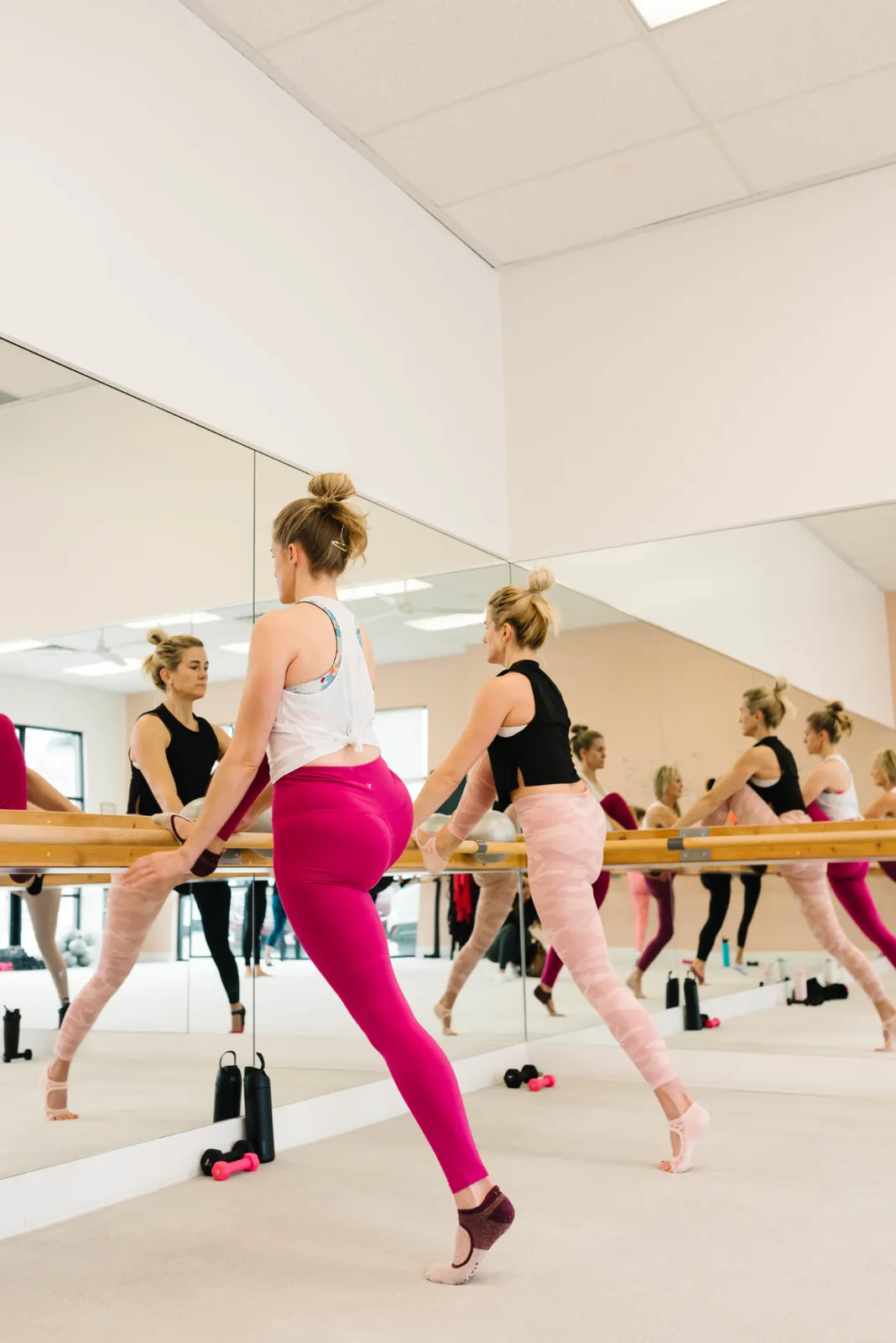 A client in pink leggings at the barre with her reflection repeating through the mirrors
