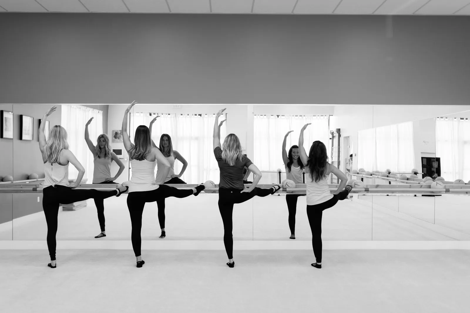 Black and white photo of four women stretching one leg on the barre in the Karve studio