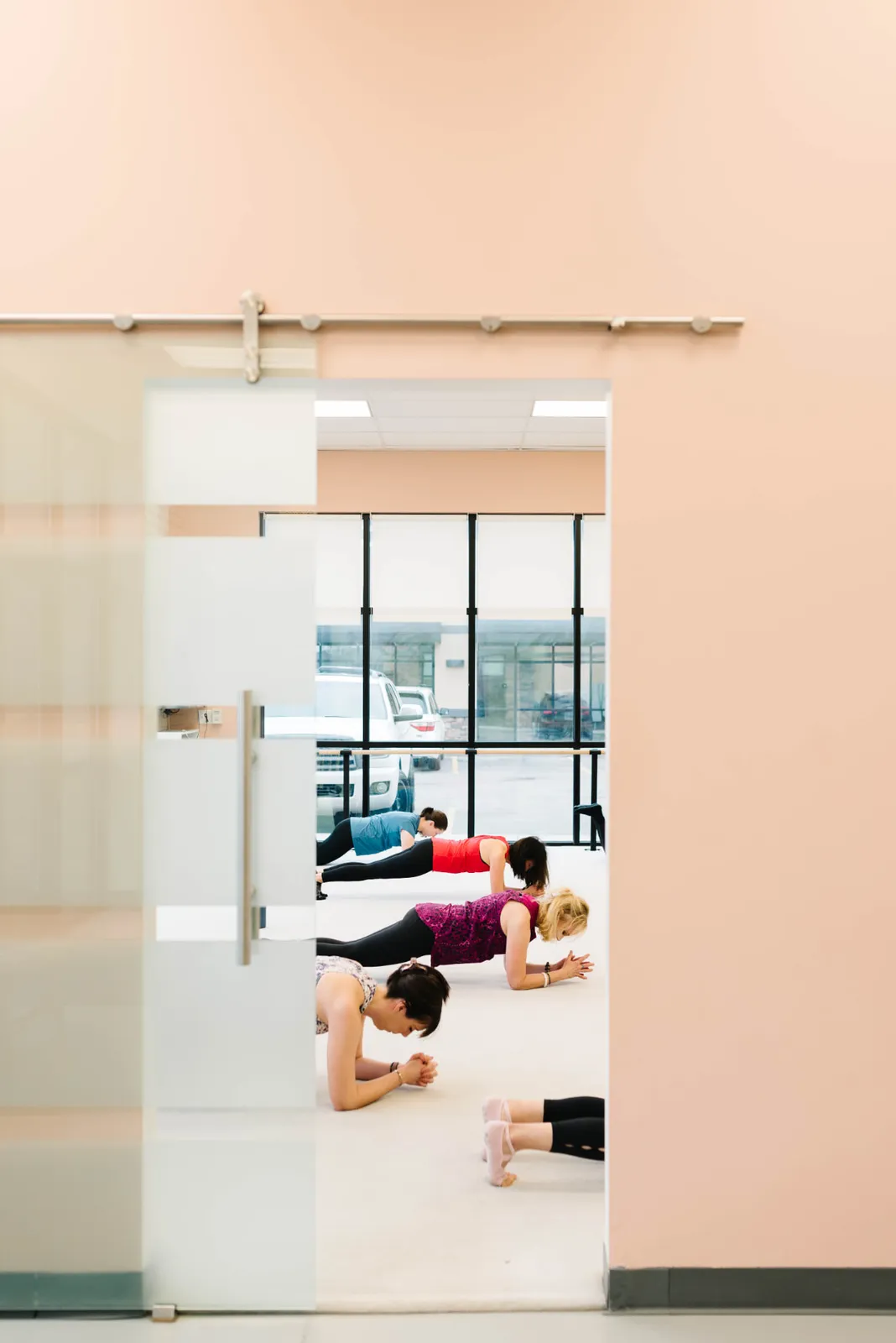 A class holding plank on the studio floor, seen through the frosted sliding door