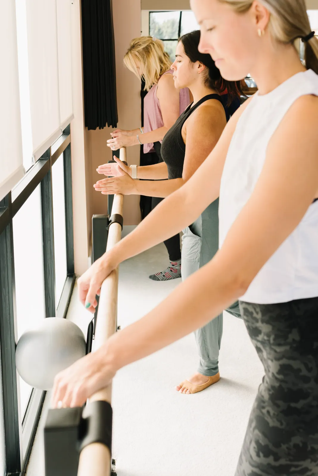A line of clients at the window barre with hands resting lightly on the wood