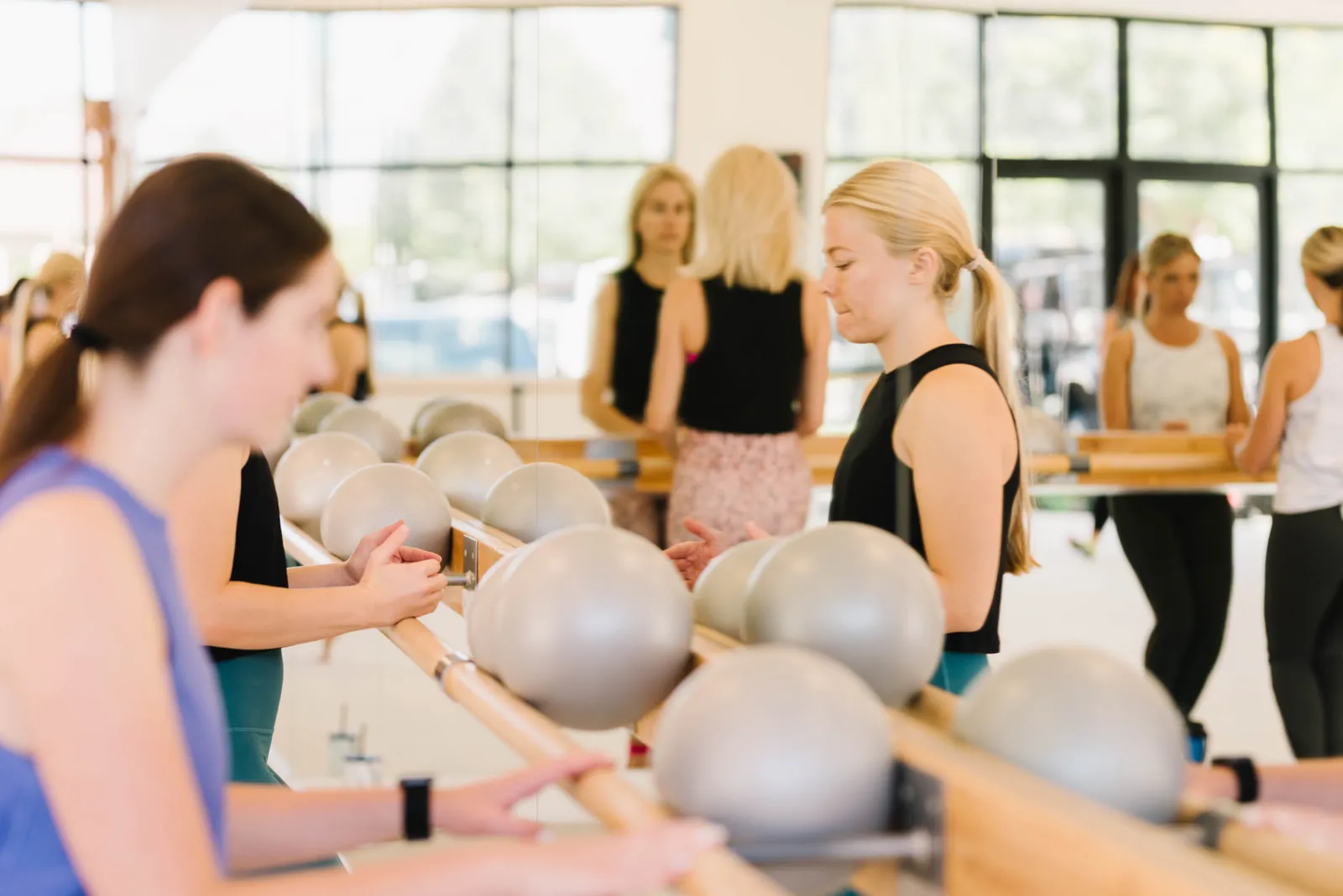 A bright class gathered along the barre with silver barre balls in position