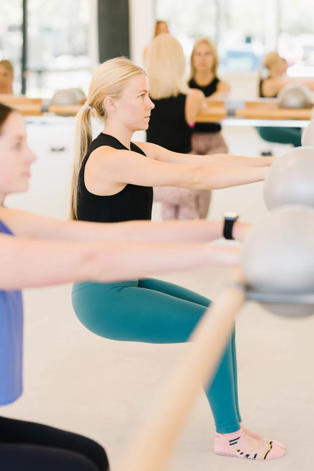A client at the barre in a black top with the class reflected in the studio mirrors